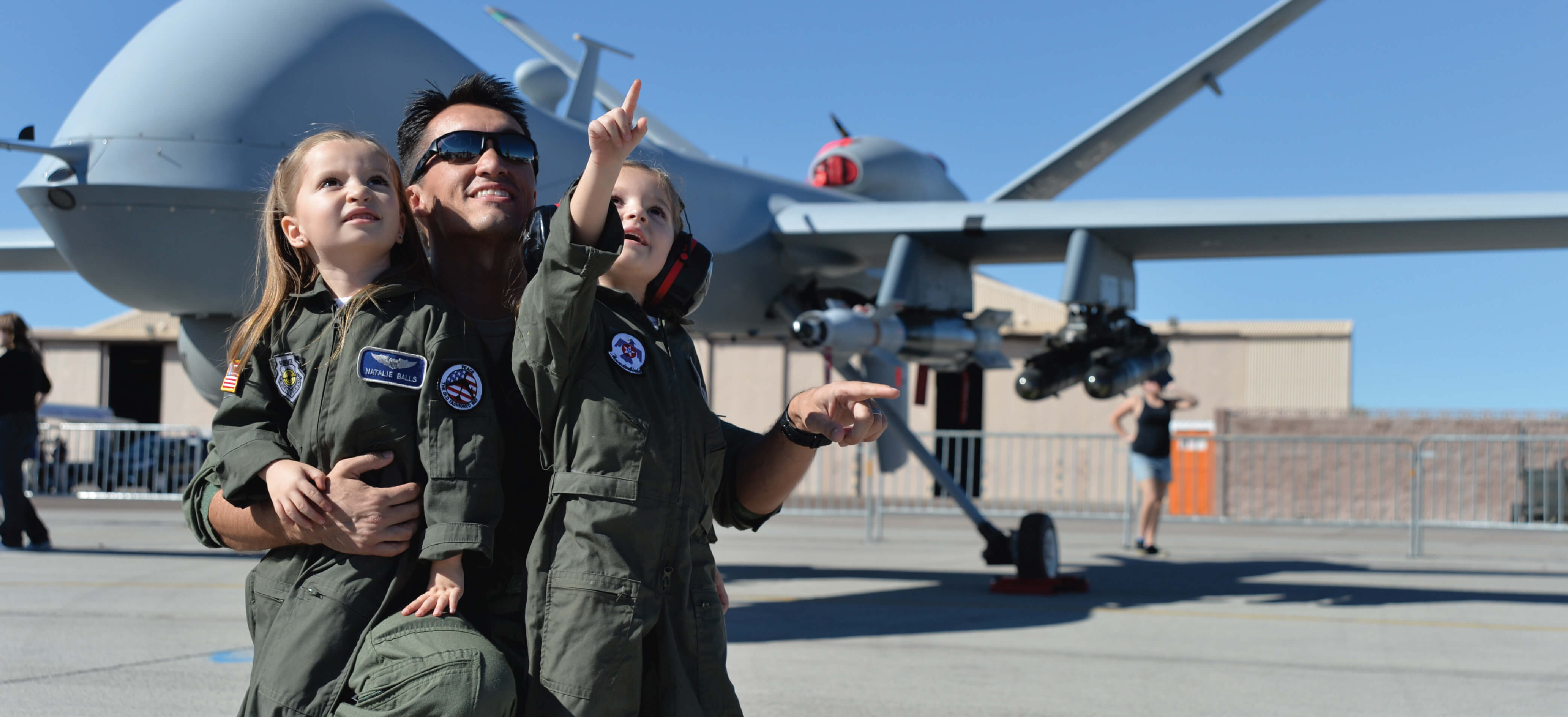 An Air Force pilot points to the sky with his daughters