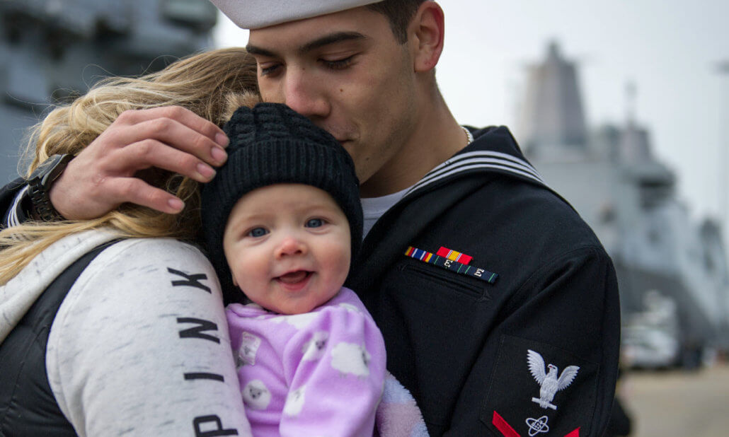 Navy family hugs near the shore