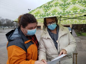 Women wearing face masks stand under umbrella at Reaching Rural Veterans event in Illinois